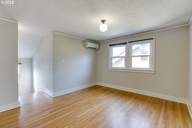 empty room with a wall mounted air conditioner, a textured ceiling, and light hardwood / wood-style flooring