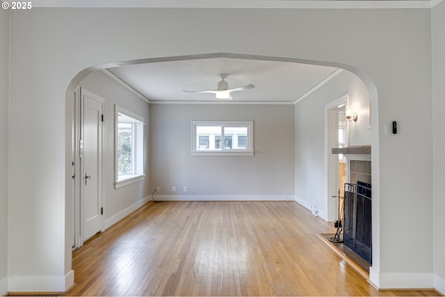 unfurnished living room featuring ornamental molding, light hardwood / wood-style flooring, a tile fireplace, and ceiling fan