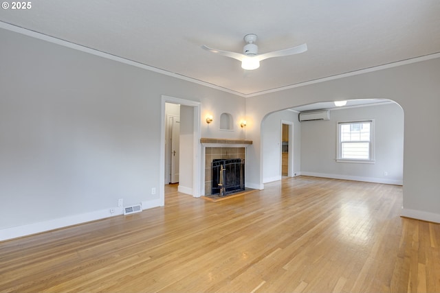 unfurnished living room with a wall mounted air conditioner, ornamental molding, ceiling fan, a fireplace, and light hardwood / wood-style floors