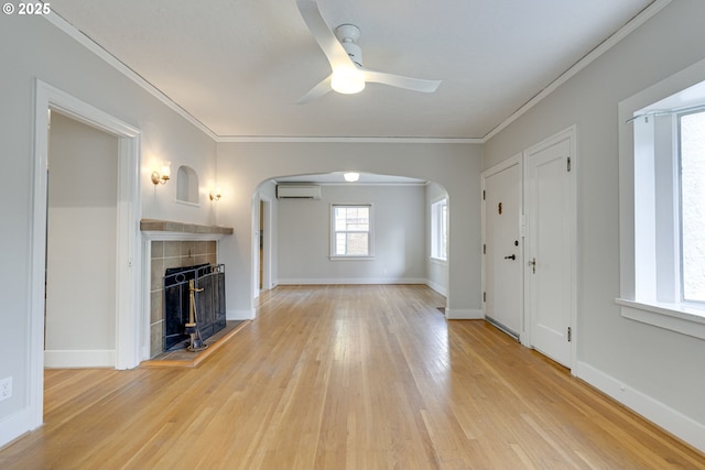 unfurnished living room with crown molding, a tiled fireplace, a wall unit AC, and light wood-type flooring