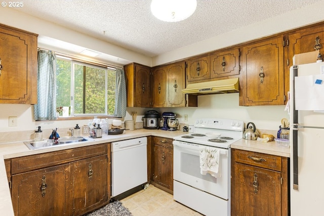 kitchen featuring white appliances, light countertops, a textured ceiling, under cabinet range hood, and a sink