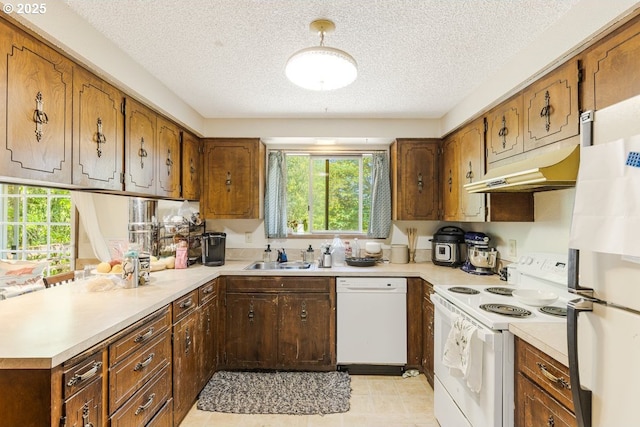 kitchen with white appliances, under cabinet range hood, a sink, and light countertops