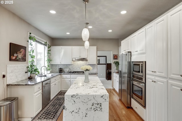 15463 NW Andalusian Way, Portland, OR 97229 - kitchen with appliances with stainless steel finishes, a sink, under cabinet range hood, a center island, and decorative backsplash