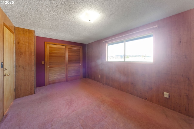 unfurnished bedroom with a textured ceiling, light colored carpet, wooden walls, and a closet