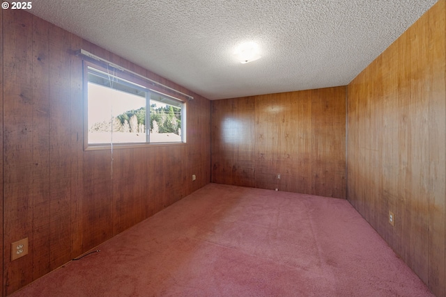 spare room featuring a textured ceiling, wooden walls, and carpet flooring