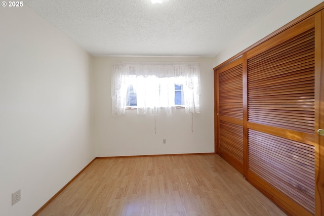 unfurnished room with light wood-type flooring and a textured ceiling