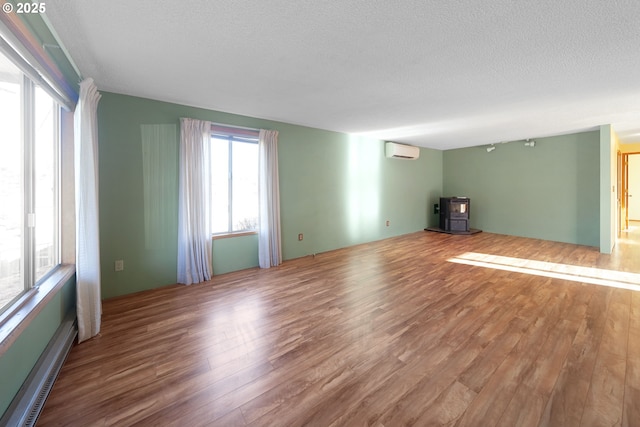 unfurnished room featuring a textured ceiling, baseboard heating, a wall mounted air conditioner, and wood-type flooring