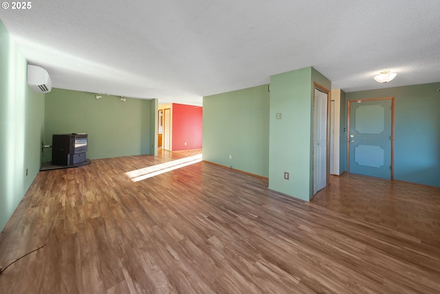 unfurnished living room with a textured ceiling, a wood stove, a wall unit AC, and wood-type flooring