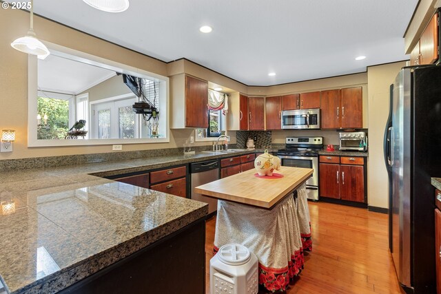 kitchen featuring appliances with stainless steel finishes, pendant lighting, sink, a center island, and light wood-type flooring