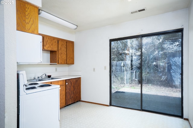 kitchen with brown cabinetry, light floors, visible vents, white electric stove, and a sink