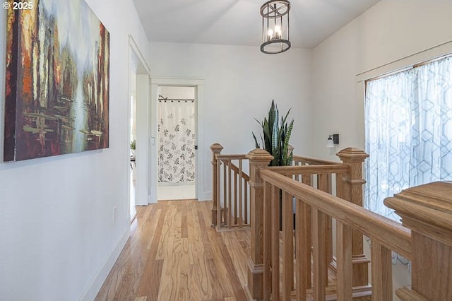 corridor with an upstairs landing, light wood-style flooring, and baseboards