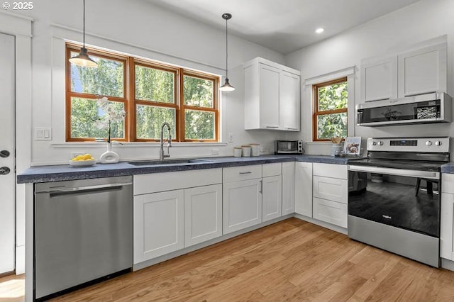 kitchen featuring stainless steel appliances, a sink, dark countertops, light wood-style flooring, and white cabinetry