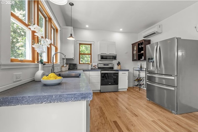 kitchen with stainless steel appliances, an AC wall unit, a sink, white cabinets, and light wood-style floors