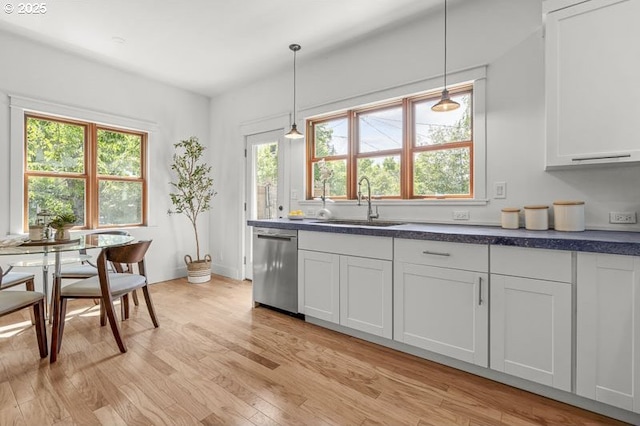 kitchen featuring dishwasher, a sink, light wood-type flooring, dark countertops, and pendant lighting
