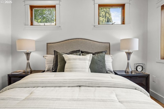 bedroom with multiple windows, wood finished floors, and baseboards