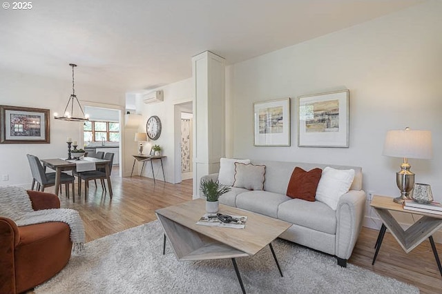 living room with wood finished floors, a chandelier, an AC wall unit, and baseboards