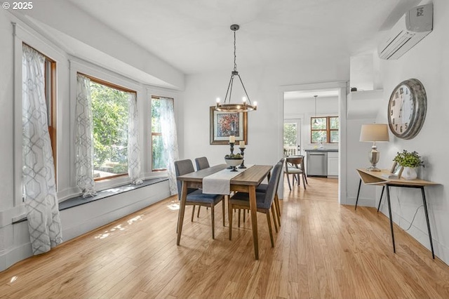 dining area featuring a wall unit AC, a chandelier, and light wood-style floors