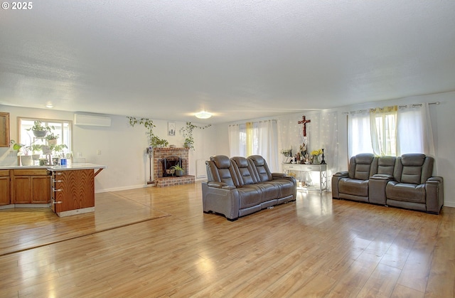 living room with an AC wall unit, a brick fireplace, light wood-type flooring, and a textured ceiling