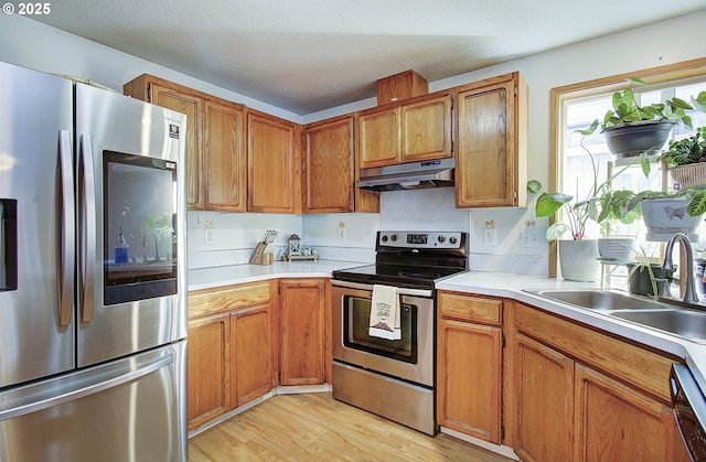 kitchen featuring sink, a textured ceiling, light wood-type flooring, and appliances with stainless steel finishes