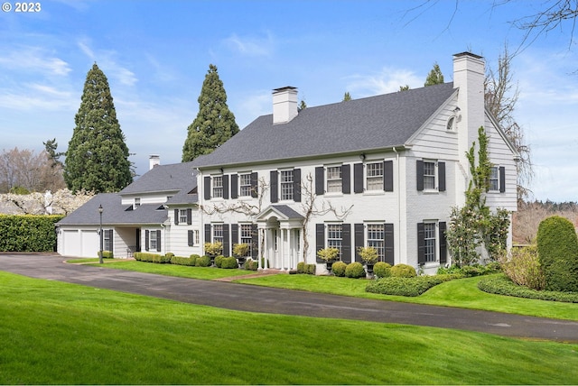 view of front of property with an attached garage, a chimney, and a front lawn