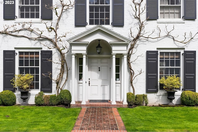 entrance to property featuring a lawn and brick siding