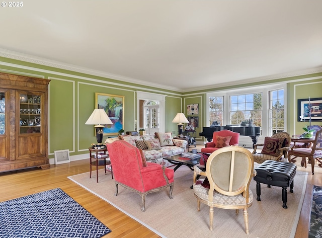 living room featuring light wood finished floors, visible vents, a decorative wall, and ornamental molding