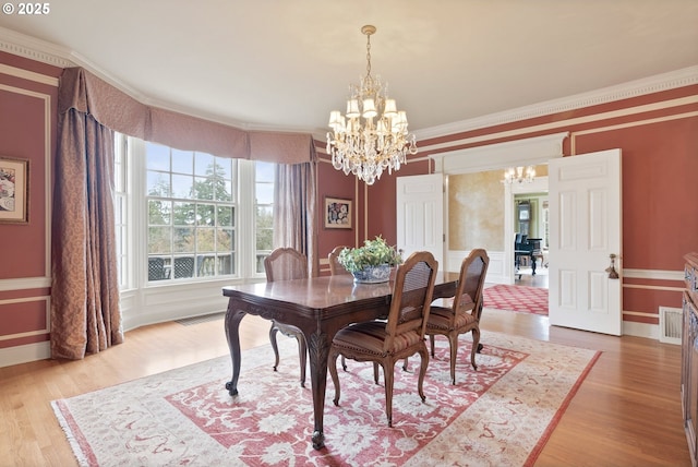 dining area with a chandelier, a decorative wall, visible vents, ornamental molding, and light wood finished floors