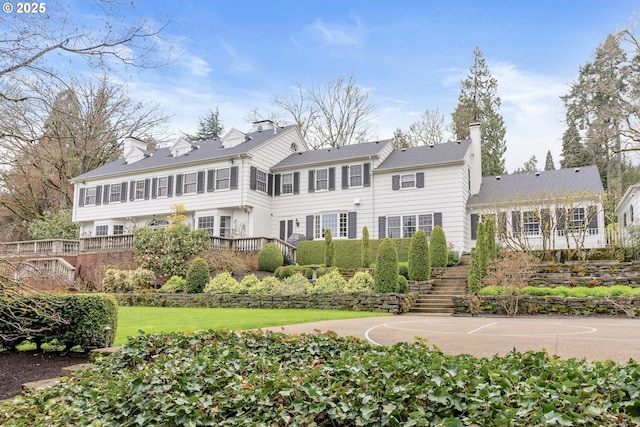 rear view of property featuring stairs, community basketball court, a chimney, and a yard