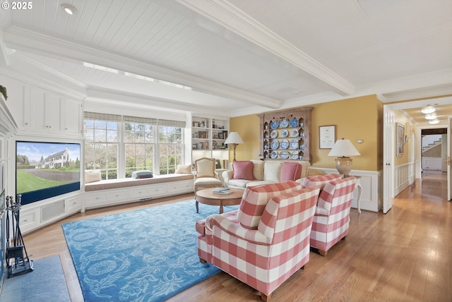 living area with crown molding, light wood-type flooring, wainscoting, and beamed ceiling