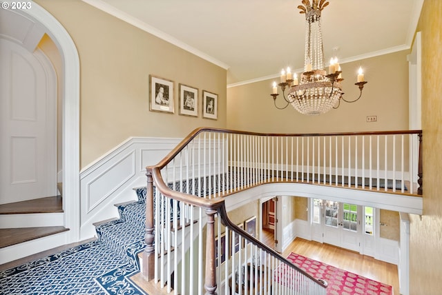 stairs with arched walkways, wood finished floors, crown molding, a chandelier, and a decorative wall