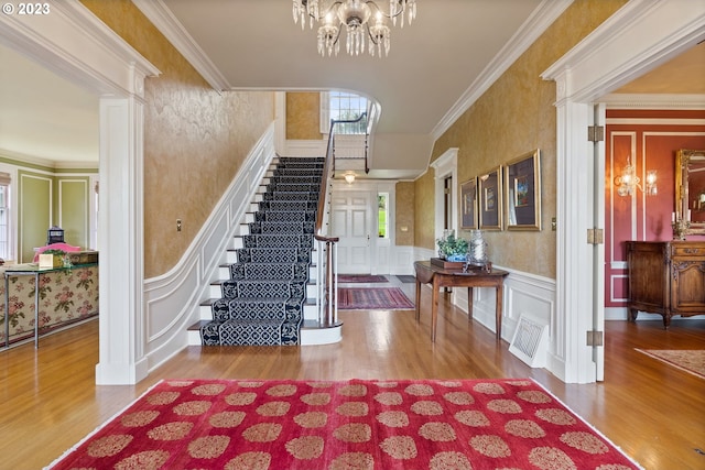 foyer entrance featuring a chandelier, visible vents, a decorative wall, and crown molding