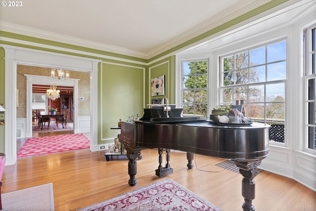 living area with a decorative wall, a wainscoted wall, wood finished floors, ornamental molding, and an inviting chandelier