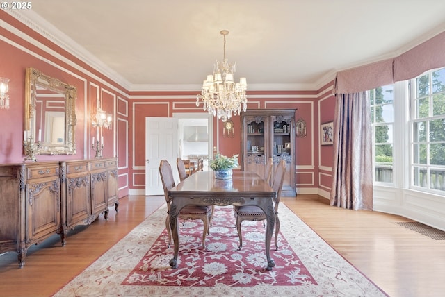 dining space with a notable chandelier, a decorative wall, visible vents, light wood-style floors, and ornamental molding