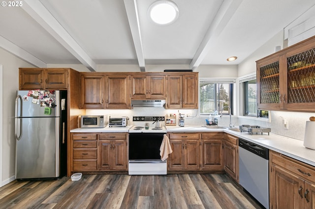 kitchen with under cabinet range hood, dark wood-type flooring, a sink, appliances with stainless steel finishes, and beamed ceiling