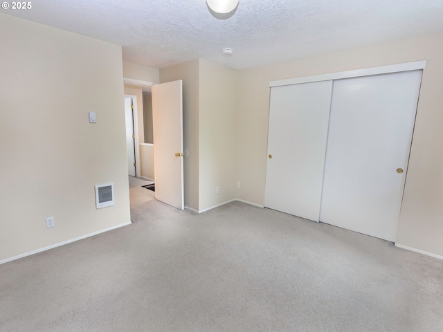 unfurnished bedroom with baseboards, a closet, light carpet, a textured ceiling, and visible vents