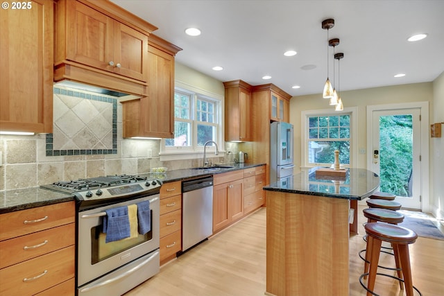 3034 NE Tillamook St, Portland, OR 97212 - kitchen featuring stainless steel appliances, a kitchen breakfast bar, dark stone countertops, light wood-type flooring, and recessed lighting