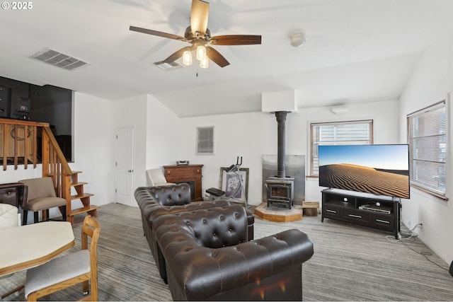 carpeted living room with a wood stove, visible vents, ceiling fan, and vaulted ceiling