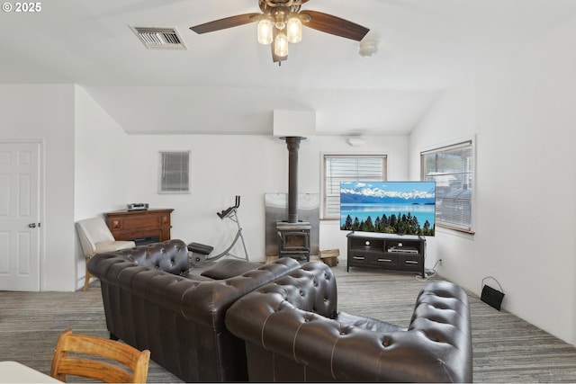 living room featuring visible vents, a wood stove, a ceiling fan, and vaulted ceiling