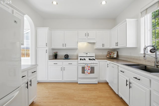 kitchen featuring white appliances, a sink, recessed lighting, under cabinet range hood, and white cabinets
