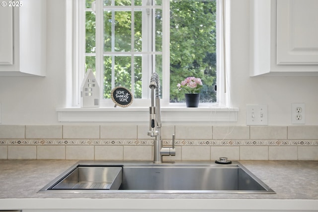 kitchen view of a sink, backsplash, white cabinetry, and light countertops