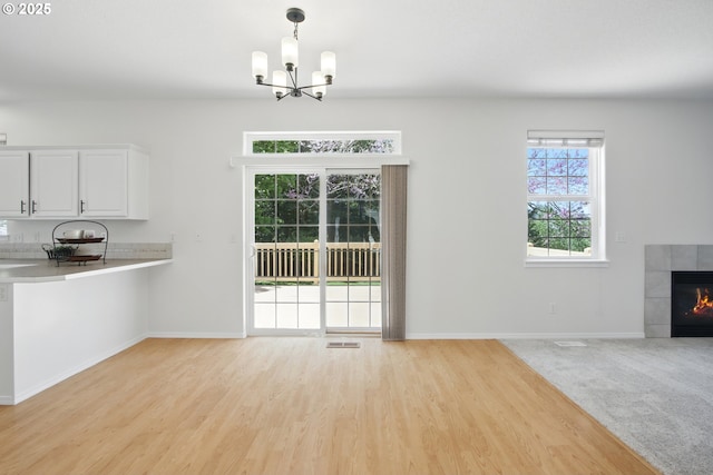 unfurnished dining area featuring a chandelier, light wood finished floors, baseboards, and a tile fireplace