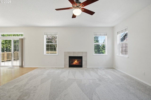 unfurnished living room with carpet floors, a tile fireplace, baseboards, and a ceiling fan