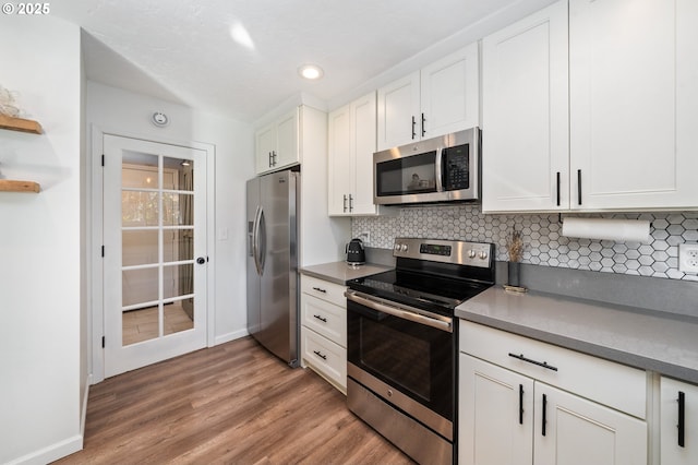 kitchen featuring stainless steel appliances, white cabinetry, baseboards, light wood-type flooring, and tasteful backsplash