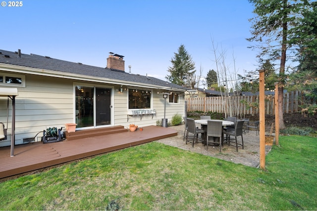 back of property featuring fence, a chimney, a wooden deck, and a lawn