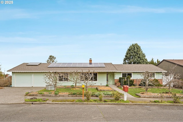 ranch-style home featuring fence, solar panels, an attached garage, a shingled roof, and concrete driveway