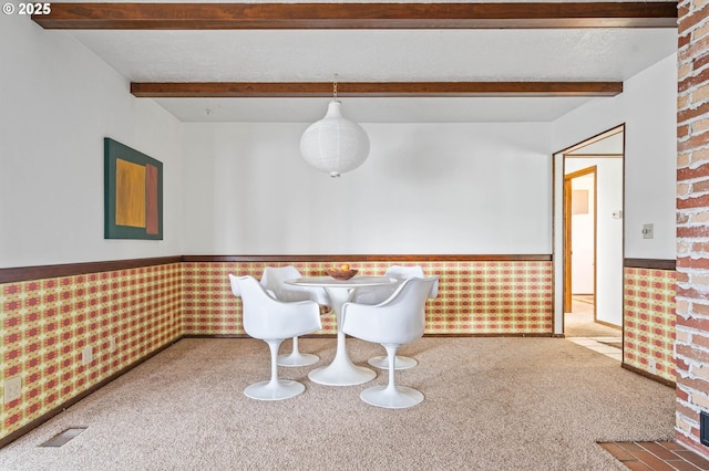 unfurnished dining area with beamed ceiling, carpet flooring, and wainscoting