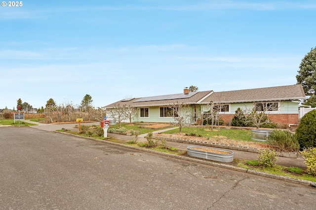 ranch-style home with brick siding, roof mounted solar panels, and a chimney