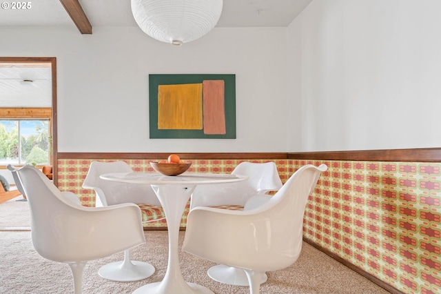 dining space featuring beamed ceiling, carpet flooring, and wainscoting