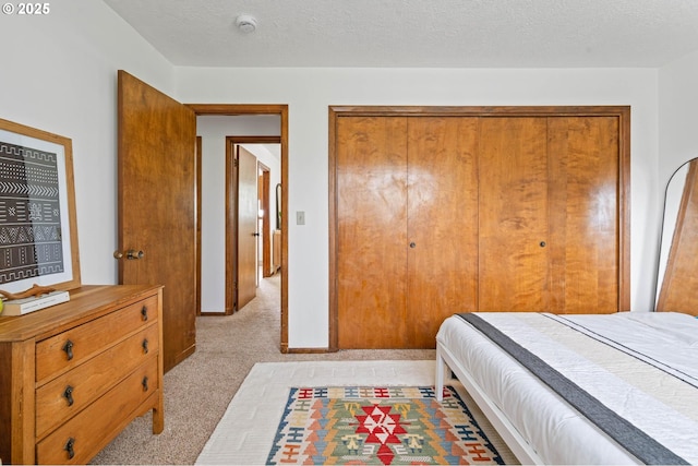 bedroom featuring light carpet, baseboards, a textured ceiling, and a closet