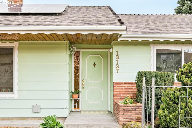 view of exterior entry with roof mounted solar panels and roof with shingles